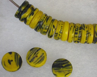 May include: A strand of yellow and black beads with a striped pattern. The beads are round and flat, with a hole running through the center. Three loose beads are also visible.