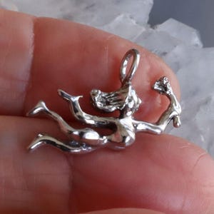 May include: A silver pendant depicting a stylized figure, possibly a mermaid or nymph, with flowing hair and outstretched arms. The pendant is detailed and appears to be made of a shiny metal.