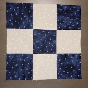 May include: A patchwork quilt block with a checkerboard pattern of white fabric with small white stars and blue fabric with small white stars.