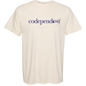 Könnte beinhalten: Ein cremefarbenes T-Shirt mit dem Text "codependent" in Blau auf der Vorderseite.