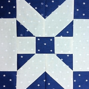 May include: Close-up of a quilt block with a geometric design. The block features a combination of white fabric with small polka dots and navy blue fabric with white stars. The design creates a star-like pattern.