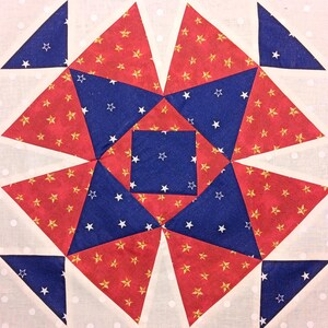May include: A close-up of a quilt block with a starburst design. The block features red fabric with gold stars, blue fabric with white stars, and white fabric with small polka dots. The design is geometric.