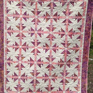 May include: A quilt with a white background and a pattern of pink and purple triangles. The quilt is edged with a purple and gold fabric.