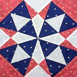 May include: Close-up of a quilt block featuring a starburst design. The block is composed of red fabric with gold stars, white fabric with small white dots, and blue fabric with white stars. The design is symmetrical.