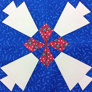 May include: Close-up of a quilt block with a patriotic theme. The design features a blue background with white stars, cream-colored triangles, and red diamond shapes with white star patterns. A central pinwheel design is visible.