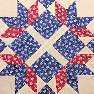 May include: Close-up of a quilt block featuring a starburst design. The quilt block has a cream-colored background with red and blue star-patterned fabric. The design is geometric and symmetrical, with a patriotic theme.