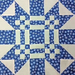 May include: Close-up of a quilt block featuring a geometric design. The quilt block has a blue star pattern on a white background. The design includes triangles, squares, and rectangles.
