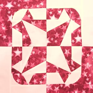 May include: A close-up of a quilt block with a geometric design. The block features a square shape with a central design of white and red star-patterned fabric. The design is composed of triangles and curved edges.