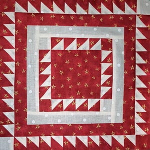 May include: A square quilt block featuring a red fabric with gold stars. White triangles and a white dotted border frame the central design. The patchwork quilt block is made from various fabrics.