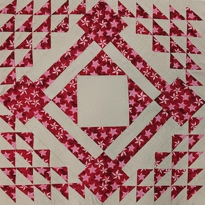 May include: A square quilt block with a geometric design. The block features a central square and a diamond shape, both in a light beige color. The diamond is outlined with red fabric patterned with white stars. Triangles in red and pink are in the corners.