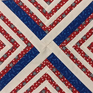 May include: A square quilt block with a patriotic design. The block features alternating stripes of red fabric with white stars, blue fabric with white stars and shooting stars, and off-white fabric. The design creates a geometric pattern.