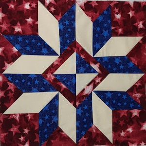May include: A square quilt block featuring a star design. The block is composed of red fabric with white stars, blue fabric with blue stars, and off-white fabric. The star is formed by the arrangement of the fabric pieces.