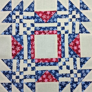 May include: A close-up of a quilt block with a repeating geometric pattern. The design features squares, triangles, and rectangles in cream, navy blue, and red. The blue and red fabrics are patterned with white stars.