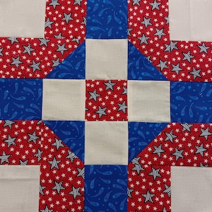 May include: A patchwork quilt block featuring a star and stripe pattern in red, white, and blue. The design includes red fabric with white stars, blue fabric with white shooting stars, and solid white squares.