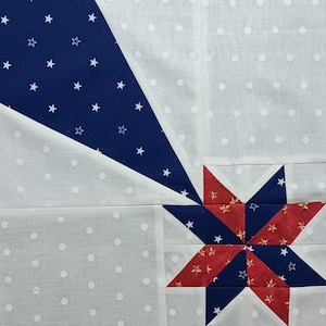 May include: Close-up of a quilt block featuring a starburst design. The block combines white fabric with small polka dots, navy blue fabric with white stars, and red fabric with gold stars. The design is geometric and patriotic.