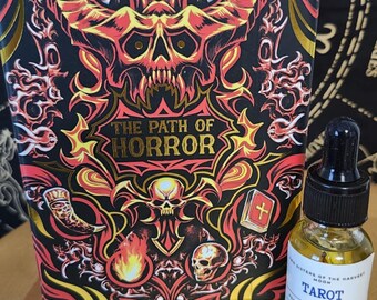 Könnte beinhalten: Eine Tarotkartenbox mit einem Schädel- und Flammendesign und dem Text "THE PATH OF HORROR". Daneben eine kleine Flasche Tarotöl mit einer Pipette. Die Box ist schwarz, rot und goldfarben.