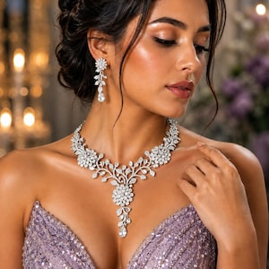 May include: A silver-toned necklace and matching drop earring set featuring clear, faceted stones arranged in a floral and leaf-inspired pattern. The necklace has a central pendant drop, and the earrings are elongated with a single floral stud.
