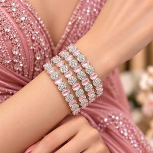 May include: A set of four matching bracelets featuring alternating oval-shaped light pink stones and circular clusters of small clear white crystals set in a silver-toned metal frame, worn together to create a layered appearance on the wrist.