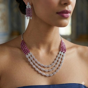 Puede incluir: Un conjunto de collar y pendientes a juego. El collar presenta una combinación de pequeñas piedras preciosas de color rojo intenso y un diseño ovalado plateado. Los pendientes tienen un diseño similar, con una cascada de piedras rojas.