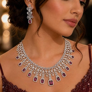 May include: A dazzling jewelry set featuring a necklace and matching earrings. The necklace and earrings are adorned with sparkling clear stones and rectangular, deep red gemstones. The jewelry is set against a dark background.