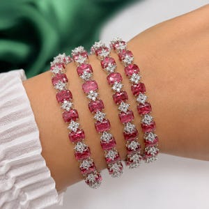 May include: Four bracelets featuring pink, rectangular gemstones and small white gemstones. The bracelets are displayed on a wrist. The gemstones are set in a silver or white metal. The background includes a white shirt sleeve.