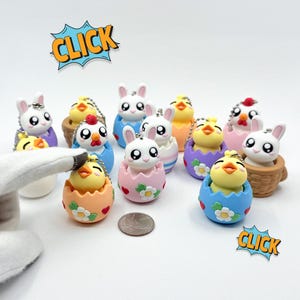 May include: A collection of Easter-themed keychains featuring chicks and bunnies emerging from colorful eggs and baskets. The keychains are in various colors, including blue, pink, orange, and yellow. The word "CLICK" is in a comic book style speech bubble.