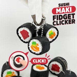 May include: Three sushi maki fidget clicker keychains with black seaweed exteriors and white rice centers featuring red, orange, and green fillings. The text SUSHI MAKI FIDGET CLICKER is displayed in red and black. A small inset shows a finger pressing the center.