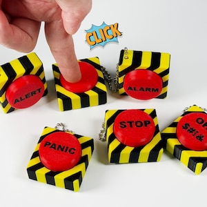 May include: A collection of novelty push button keychains. Each square button is yellow and black striped with a red button. The buttons have the words "ALERT", "ALARM", "STOP", "PANIC", and "OH $#!&" printed on them.