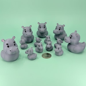 May include: A collection of gray hippo figurines of various sizes, including a duck-shaped hippo, arranged on a light green surface. A coin is placed among the figurines. The hippos have black eyes and pink ears.