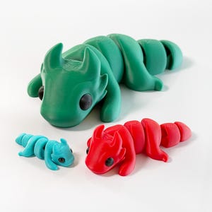 May include: Three 3D printed dragon figurines in different sizes. The largest dragon is green, the medium dragon is red, and the smallest dragon is blue.