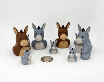 May include: A collection of small donkey-shaped figurines in varying sizes, rendered in shades of brown and gray with light-colored muzzles. A United States quarter coin is placed in the center for scale, showing the relative size of the figures.