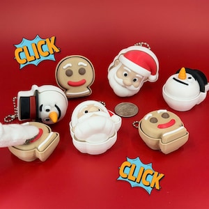 May include: A collection of Christmas-themed keychains in the shape of Santa Claus, a snowman, and gingerbread men. The keychains are white, red, brown, and black, with a silver chain. The word "CLICK" is in a speech bubble.
