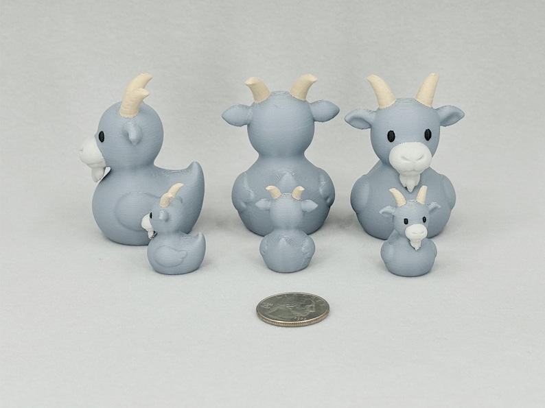 May include: A collection of light blue goat figurines with cream-colored horns and beards. The set includes three larger goats and three smaller ones, with a quarter coin for size comparison. The goats have a whimsical, cartoonish design.