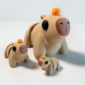 May include: Three beige capybara figurines with orange accents. The largest capybara is sitting with its legs outstretched. The middle capybara is sitting with its legs tucked under its body. The smallest capybara is standing with its legs together.