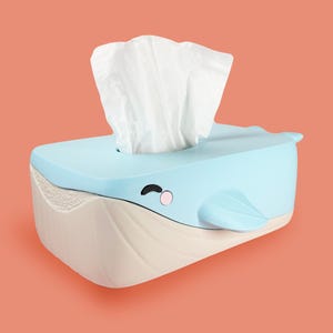 May include: A light blue whale-shaped tissue box with a white tissue protruding from the top. The box has a light beige base and a cartoon whale face with a pink cheek and black eye.