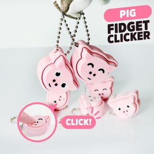 May include: Pink pig-shaped fidget clickers on silver chains. The image includes the text "PIG FIDGET CLICKER" and a close-up showing the clicker being pressed. The clickers have black eyes and a smiling mouth.