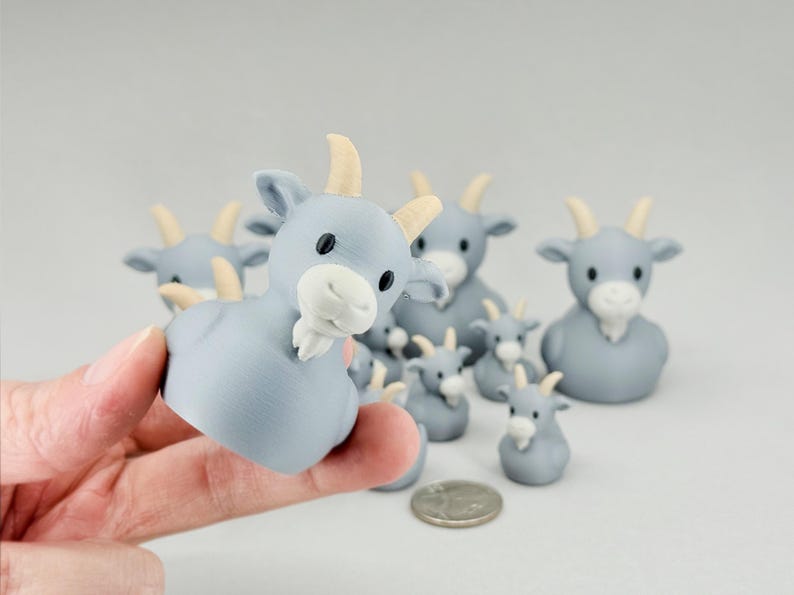 May include: A collection of light blue goat figurines with cream-colored horns and white beards. The figurines vary in size, with some held in a hand. A coin is also present.