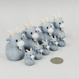 May include: A collection of light blue goat figurines with white beards and horns. The figurines vary in size, with a U.S. quarter for scale. The goats are arranged in a row, showcasing a family or herd theme.