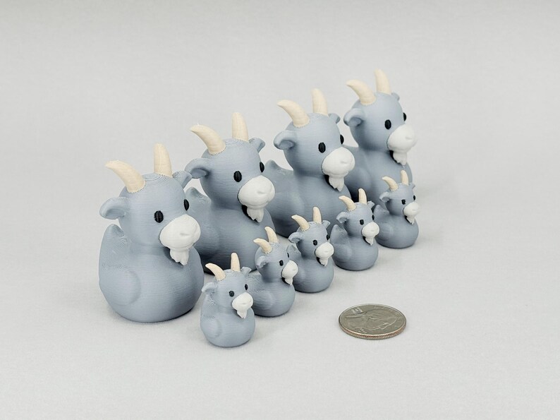May include: A collection of light blue goat figurines with white beards and horns. The figurines vary in size, with a U.S. quarter for scale. The goats are arranged in a row, showcasing a family or herd theme.