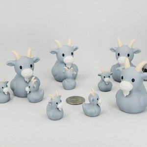 May include: A collection of light blue goat figurines with white beards and horns. The figurines vary in size, with some appearing to be baby goats. A small koala bear figurine is also present. A US quarter is included for size reference.