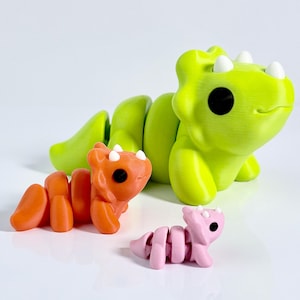 May include: Three articulated dinosaur toys in different colors. A large lime green dinosaur is in the background, an orange dinosaur in the middle, and a small pink dinosaur in the foreground. Each dinosaur has black eyes and white spikes.