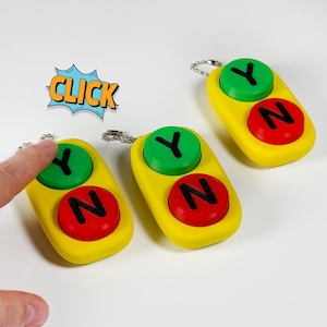May include: Three yellow keychains with a green button labeled "Y" and a red button labeled "N". The keychains are on a white surface. One keychain has a finger pressing the green button. The word "CLICK" is in a comic book style speech bubble.