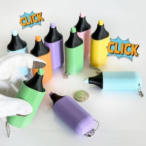 May include: A collection of colorful highlighter-shaped keychains in various colors, including green, orange, purple, and yellow. Each keychain has a black tip and a silver chain. The word "CLICK" is displayed in a comic book style.