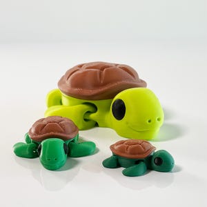 May include: Three 3D printed turtle figurines. The largest turtle is green with a brown shell and has a smiling face. The two smaller turtles are green with brown shells and have closed eyes.