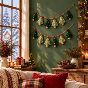K&ouml;nnte beinhalten: Zwei horizontale Girlanden mit abwechselnd dunkel- und hellgr&uuml;nen geh&auml;kelten Weihnachtsbaum-Anh&auml;ngern. Jeder Baum ist mit einer kleinen roten Schleife und wei&szlig;en Punkten verziert und an einer naturfarbenen Kordel befestigt.