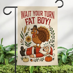 May include: A garden flag with the text "WAIT YOUR TURN FAT BOY!" features a cartoon turkey standing on Santa Claus. The flag has a beige background with illustrations of pumpkins, wheat, and a sunflower. The flag is hanging on a black metal stand.
