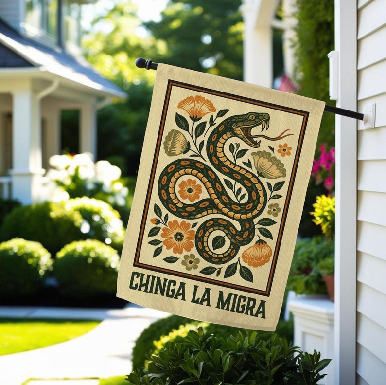 May include: A beige garden flag featuring a stylized snake design with orange and green floral accents. The flag has a dark brown border and the words "CHINGA LA MIGRA" in bold, black letters.