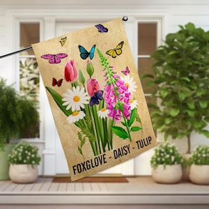 May include: A garden flag with a floral design featuring foxgloves, daisies, and tulips. The flag is beige with a brown border and has the text "Foxglove - Daisy - Tulip" printed at the bottom.