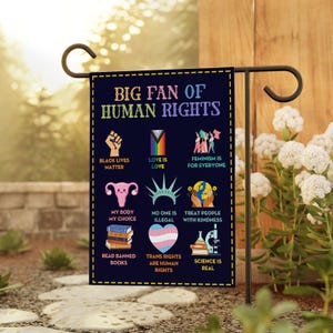 May include: A navy blue garden flag with the text "BIG FAN OF HUMAN RIGHTS" and various icons representing social justice causes, including "Black Lives Matter," "Love is Love," and "Trans Rights are Human Rights."