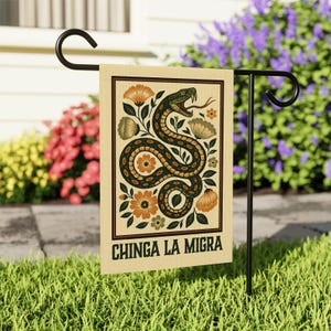 May include: A beige garden flag featuring a stylized snake design with orange and green floral accents. The snake is coiled and has its tongue out. The text "CHINGA LA MIGRA" is printed at the bottom of the flag.